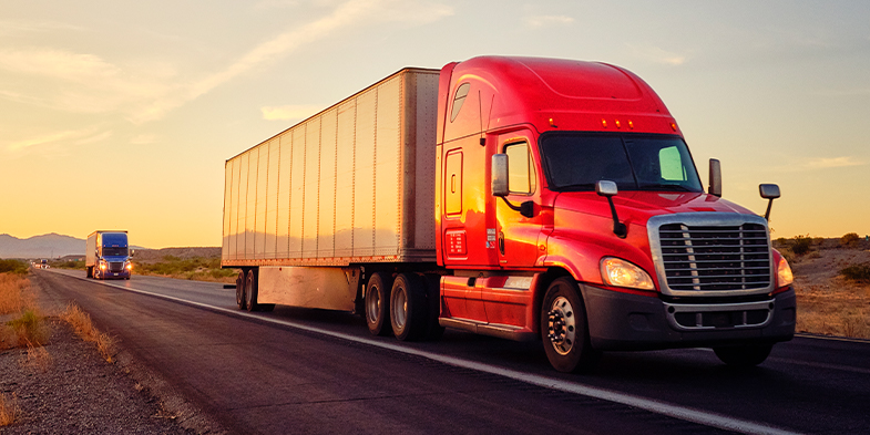 Red shipping truck driving down a highway at sunset