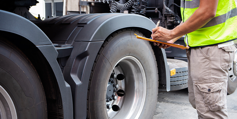 Man in a yellow safety vest standing next to a shipping truck while taking notes on a clipboard