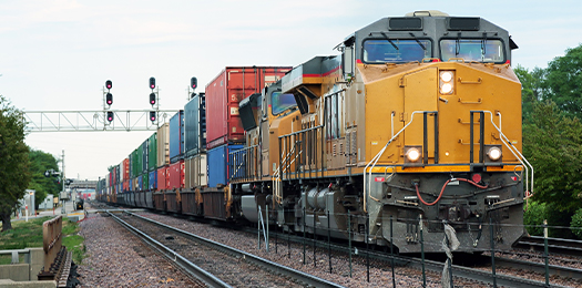 Train traveling down railroad tracks carrying shipping containers